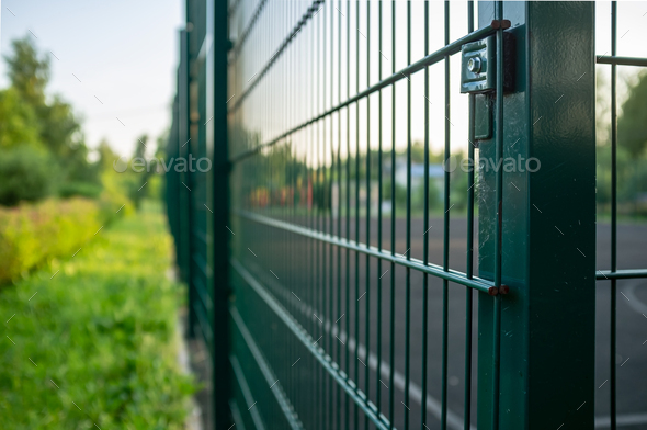 Sports ground is fenced with a green welded mesh fence, outdoors, in the evening at sunset
