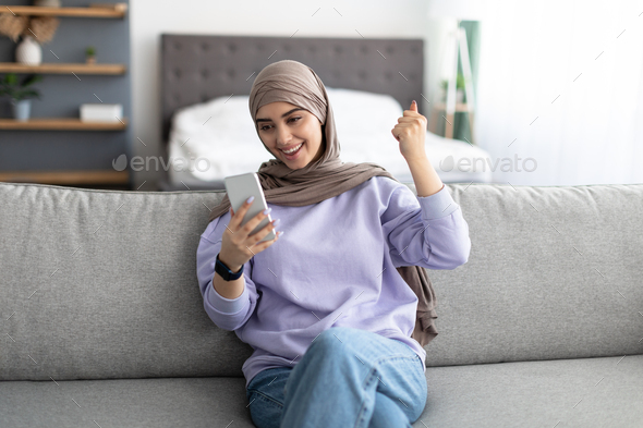 Muslim woman using cell phone celebrating success shaking fists