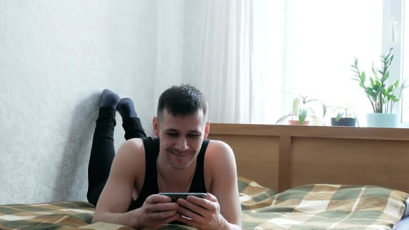 Young Guy Typing a Message on His Smartphone While Sitting on the Bed at Home