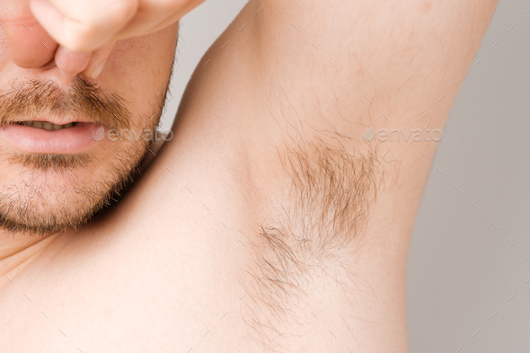 Close up of man armpit with long unshaved hair and pinching nose from sweaty bad smell