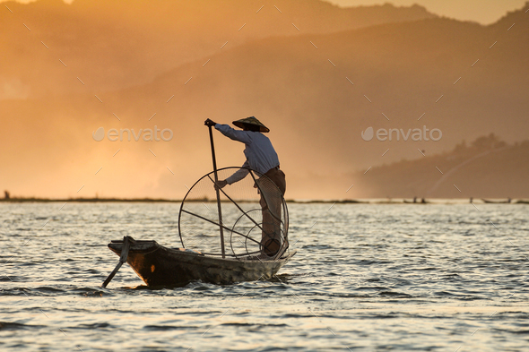 Asian Fisherman On Wooden Boat Casting A Net For Catching