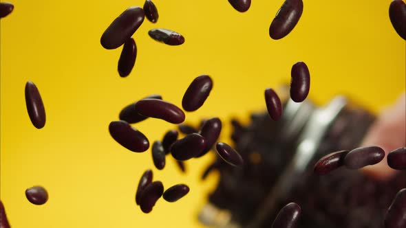 Closeup of Falling Down Red Beans on Glass Table From Jar on Yellow Background alt