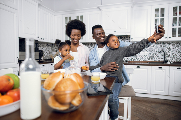 Family Using Gadgets Whilst Eating Breakfast Together In Kitchen