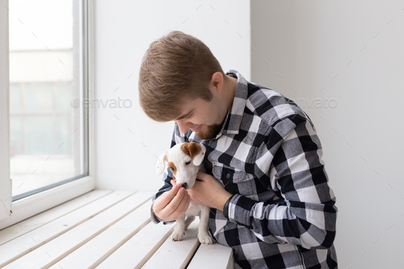 People, pet and dog concept - Young man over window background holding puppy Jack Russell Terrier