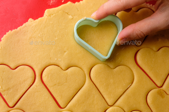 Making gingerbread cookies in heart shape using plastic cutter on the red silicon baking mat. Sweets