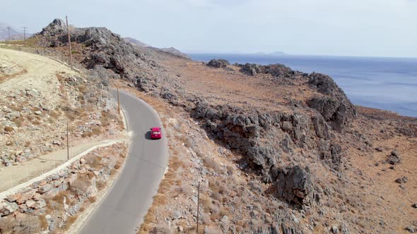 Drone shot of car driving along the narrow coastal road above rocky shore towards volcanic mountains alt