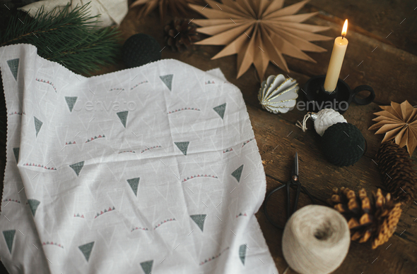 Stylish christmas gift wrapped in fabric on rustic table with scissors,  paper star, candle.Furoshiki Stock Photo by Sonyachny