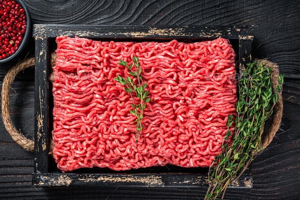 Raw mince ground beef and pork meat in a wooden tray with herbs. Black background. Top view