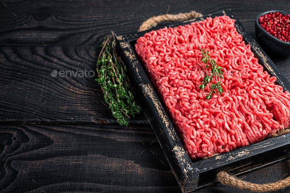 Raw mince ground beef and pork meat in a wooden tray with herbs. Black background.