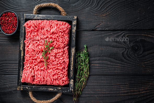 Raw mince ground beef and pork meat in a wooden tray with herbs.