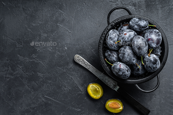 Fresh organic bio plums in a colander. Black background. Top view. Copy space