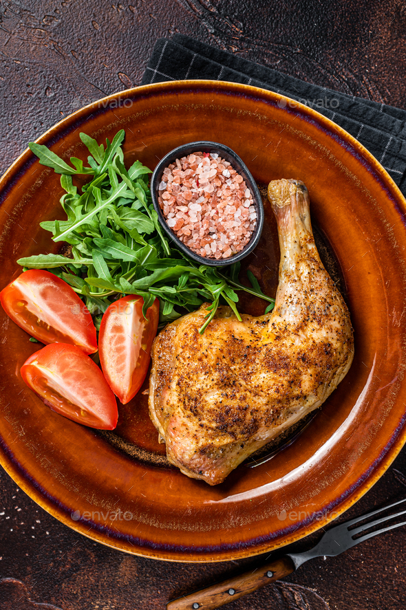 Poultry dish - roasted chicken legs with vegatables salad. Dark background. Top view