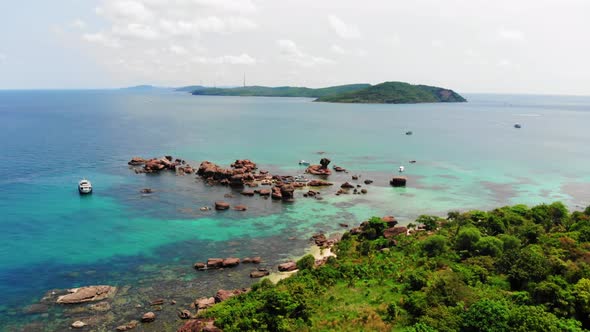 Boat Anchored in Clear Turquoise Sea Waters next to Rocks and Rocky Coast of Gam Ghi island in Vietn alt