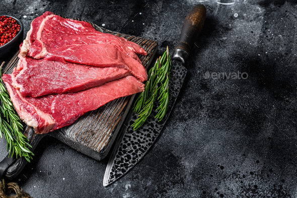 Raw fresh beef meat round steak with herbs and spices. Black background. Top view. Copy space