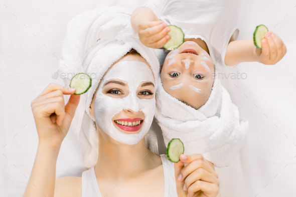 Mother and daughter in white shirts and white towels on their heads in a home bathroom, doing spa
