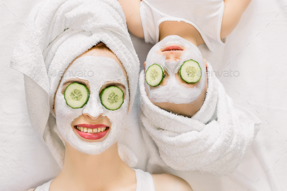 Mother and daughter doing funny spa procedures after bath. They are in white bath towels with white