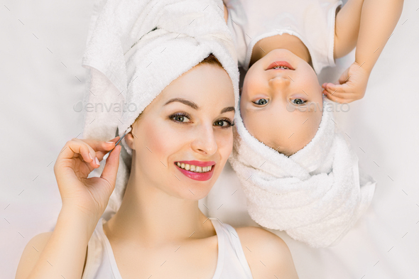 Smiling beautiful mom and daughter in a white bath towels, lying on the ...