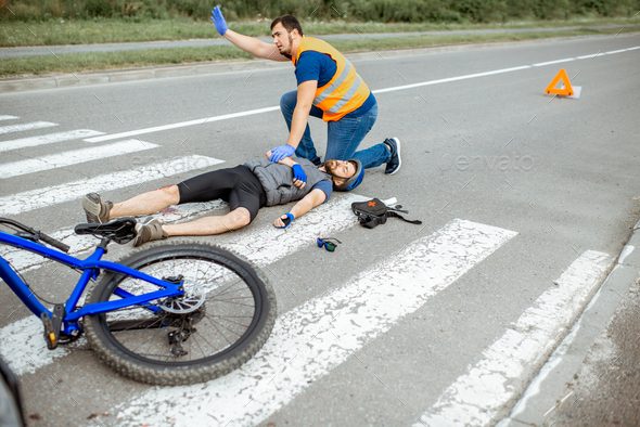 Road accident with injured cyclist and man providing first aid