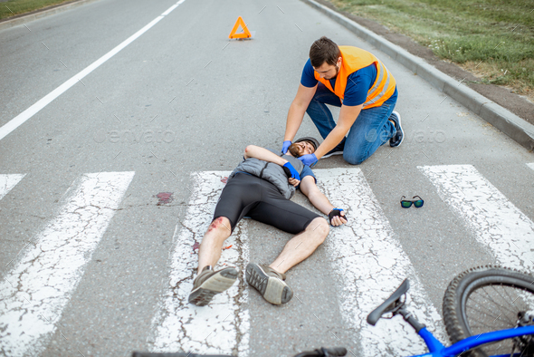 Road accident with injured cyclist and man providing first aid