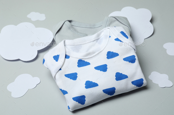 Baby clothes and decorative clouds on light gray background