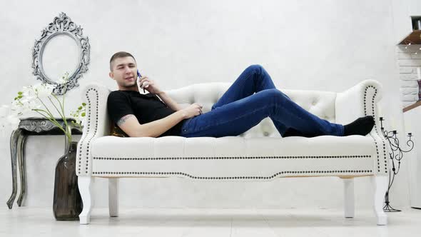 Young Man Relaxing On Couch And Speaks By Mobile Phone In Modern Young Man Relaxing On Couch And Speaks By Mobile Phone In Modern Luxury House Stock Footage