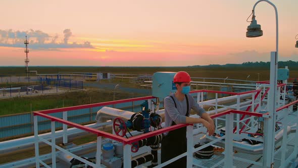 The Drone Hovers Over a Worker in a Helmet and a Mask Who is Standing on a Technological Tower in alt