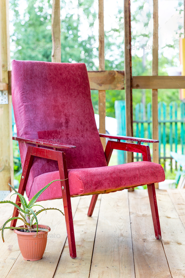 An old vintage armchair of dark pink color on an open veranda. A cozy place to read, think, relaxa