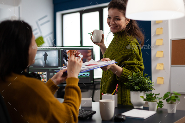Creators drinking coffee and talking during office break sitting at desk in digital agency studio
