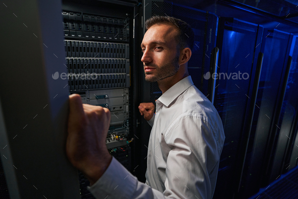 Bearded busy man technician finding and troubleshooting computer server in room indoors