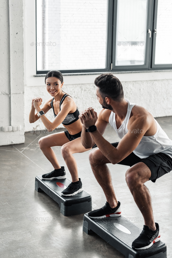 young man and woman in sportswear smiling each other while training with step platforms in gym