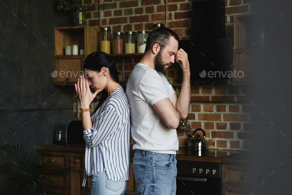 side view of young depressed couple standing back to back after quarrel at home