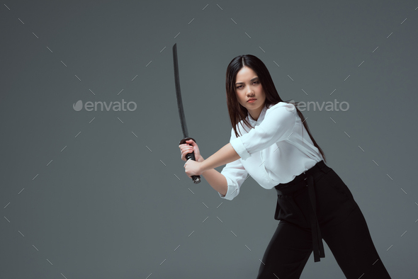young asian woman fighting with katana sword and looking at camera isolated on grey - Stock Photo - Images