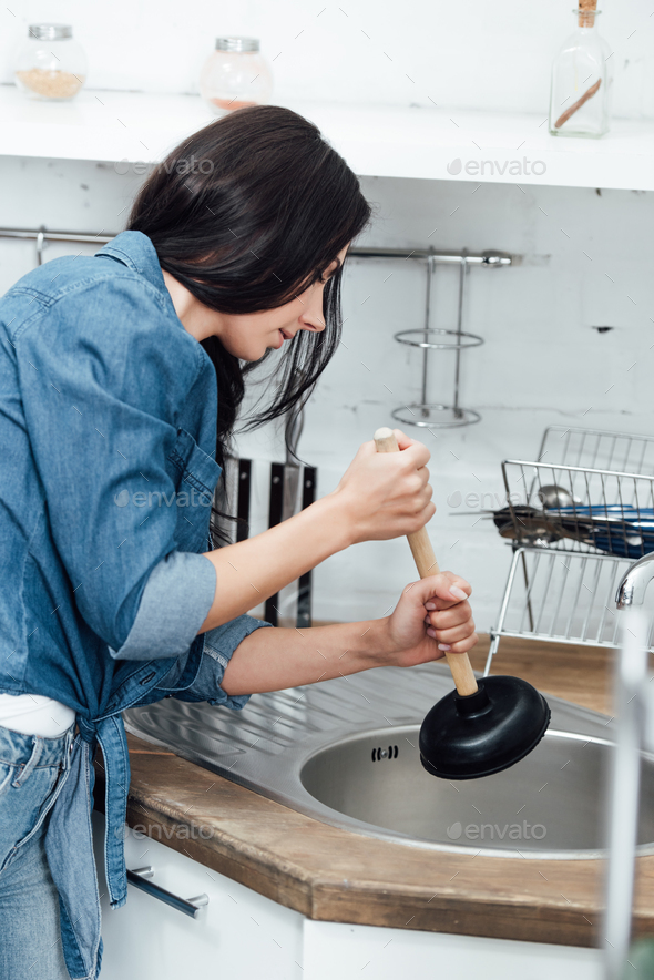 A female plumber fixing the kitchen sink with a plunger, Stock image