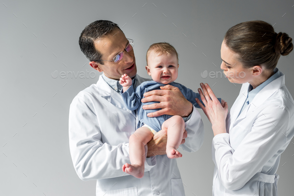 pediatricians trying to calm down little crying baby on grey