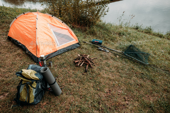 Tourist tent, backpack, fishing rods on countryside with lake