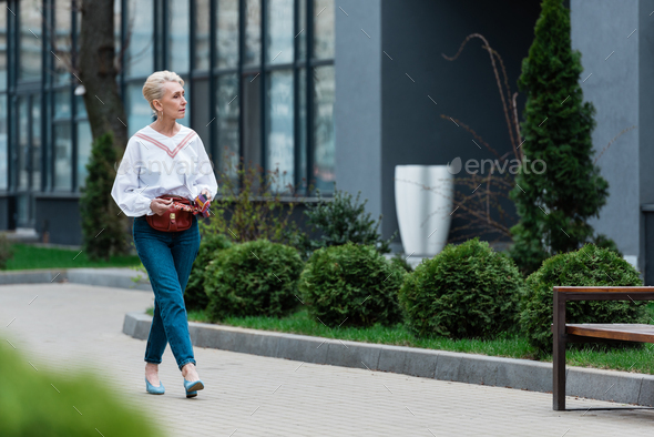 senior woman in trendy outfit with waist bag walking in park