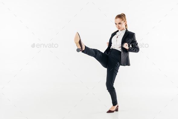 businesswoman performing karate kick in suit and high heels isolated on white