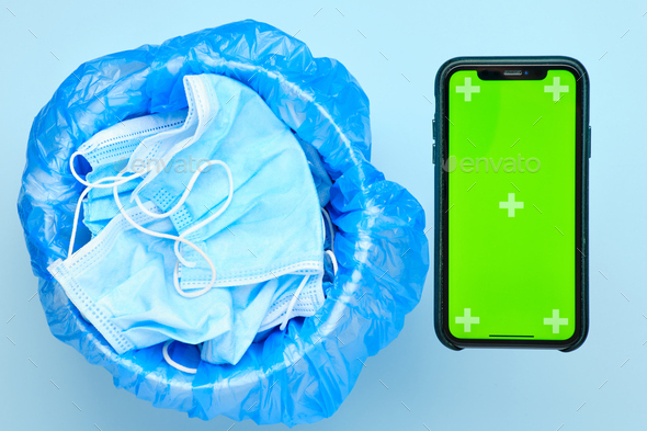 Disposable used surgical mask in a trash bin and smartphone with chroma key on a blue background