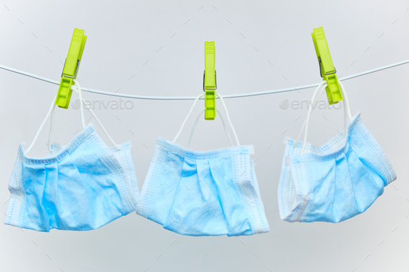 Used disposable protective surgical masks drying on a clothesline with green clothespins on a white