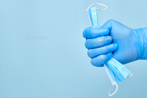 Man hand in rubber blue gloves holding used disposable protective mask on a blue background with