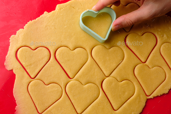 Making gingerbread cookies in heart shape using plastic cutter on the red silicon baking mat. Sweets