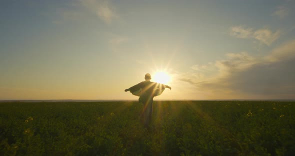 A Boy-superhero in a Green Cloak Is Running Across a Field. The Cloak Is Fluttering in the Wind alt