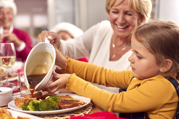 Grandmother Pouring Gravy Onto Granddaughters Food As Multi-Generation Family Eat Christmas Meal
