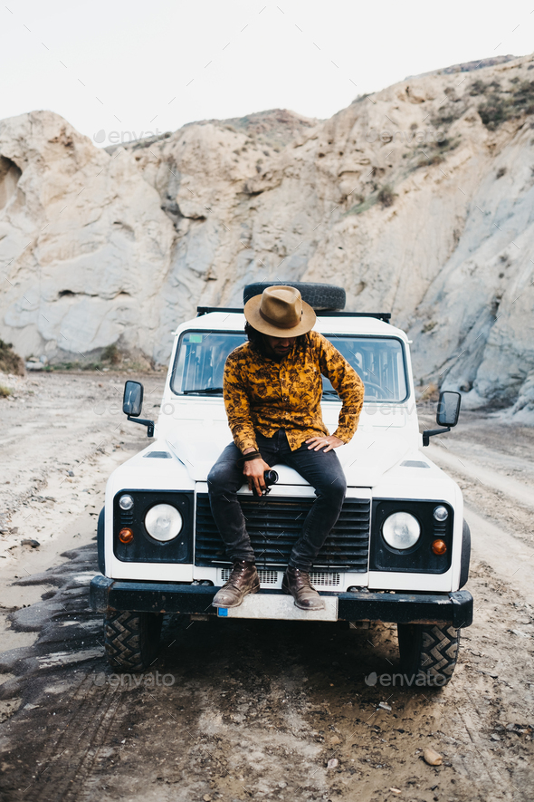 Stylish man sitting on car in canyon