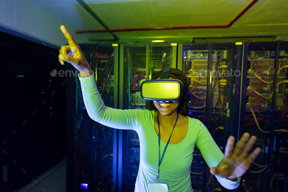 Happy african american female computer technician wearing vr headset and working in server room