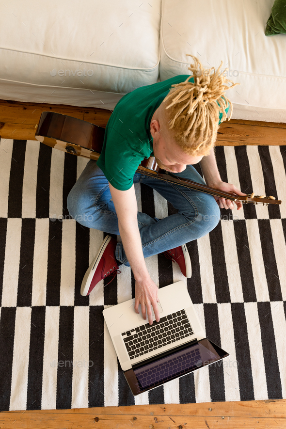 Albino african american man in the living room playing guitar and using laptop - Stock Photo - Images