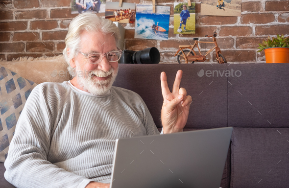 Senior attractive man using laptop in video call. Old retired man spending his time by working on pc