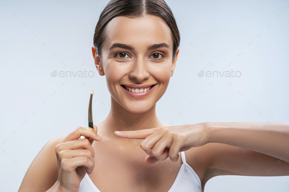 Cheerful young woman holding tweezers and smiling