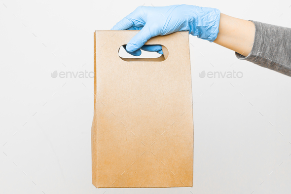 Womans hand in rubber gloves holding a cardboard bag with copy space. Concept of donation bag for