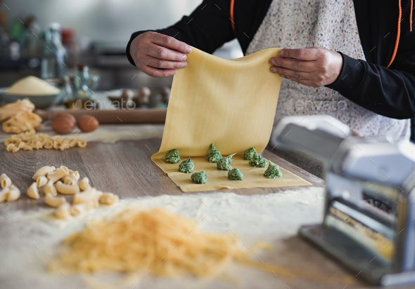 Mature woman preparing fresh made ravioli with ricotta cheese and spinach inside pasta factory
